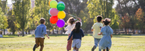 Group of children running through the grass with colorful balloons.