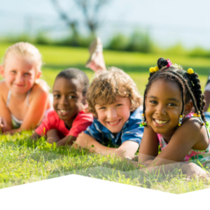 Four children laying in the grass smiling at the camera.