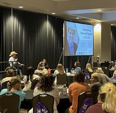 Billie Sutton speaks from stage to a room full of people seated around tables.